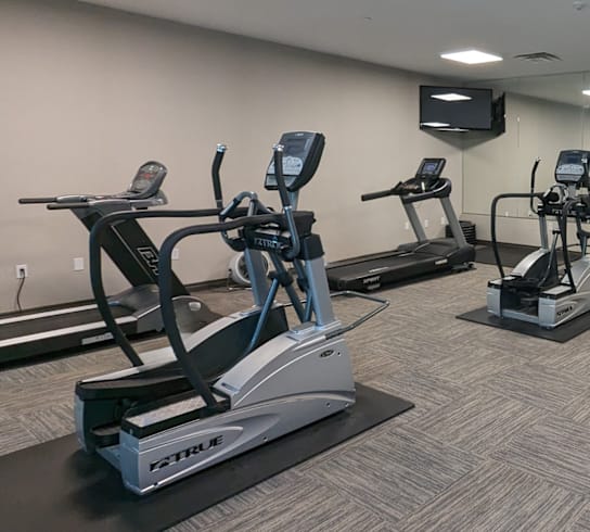 a gym with cardio equipment and a tv in a room
