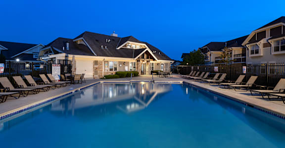 a swimming pool with chairs and a house at night