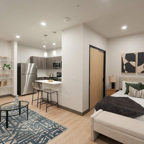 A modern bedroom with a large bed and a kitchen area in the background.