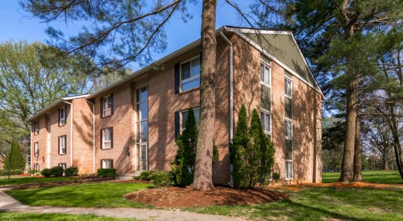 Brick apartment building with mature landscaping at The Brook At Columbia Apartments, Columbia, MD 21044
