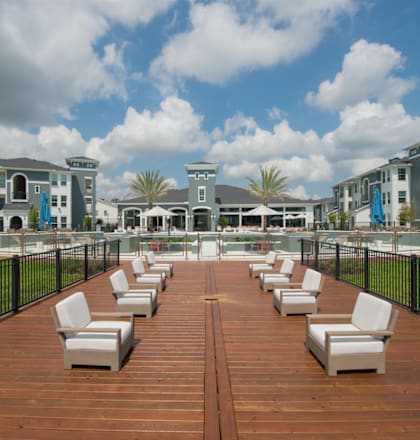 A wooden deck with white chairs and a black fence in front of apartment buildings.
