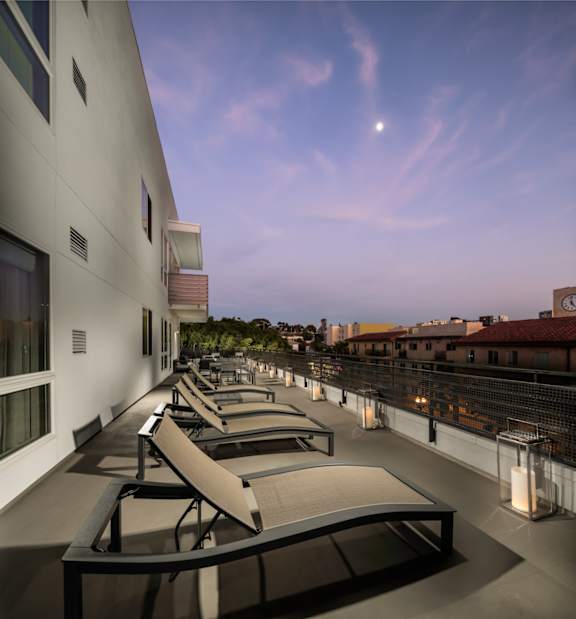 A balcony with chairs and a view of the city at dusk.