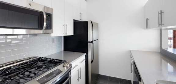 A black refrigerator sits in a kitchen with white cabinets at The Ellington Apartments, New York, NY, 10019
