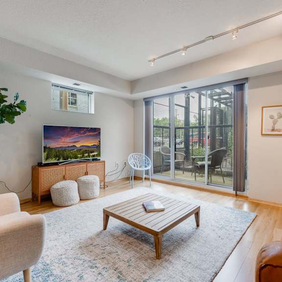 A living room with a couch, plush chair, tv, coffee table, and doors to a patio at Blue and Lime Apartments. 