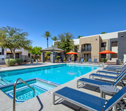 A swimming pool with sun loungers and umbrellas in front of a building.