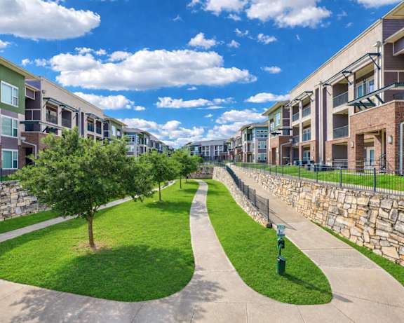 A tree is in the middle of a grassy area with apartment buildings on either side.