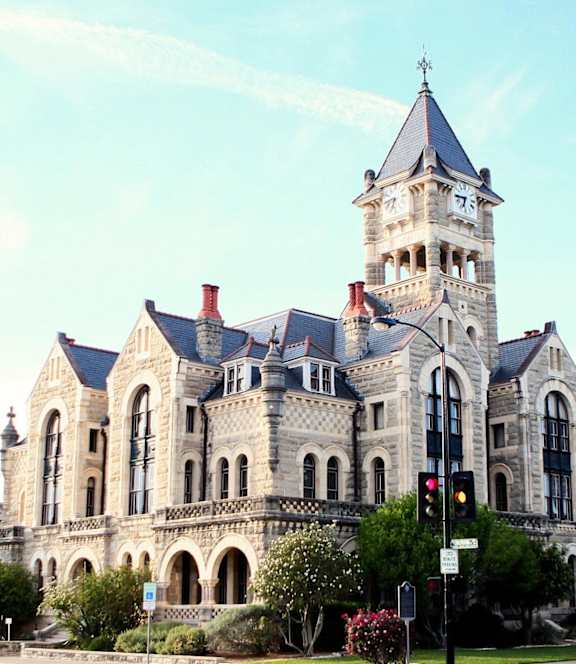 A large, ornate building with a clock tower is surrounded by greenery.