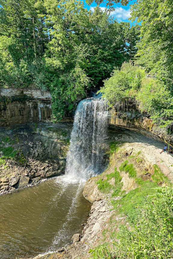 A waterfall cascades down a rocky cliff surrounded by lush greenery.