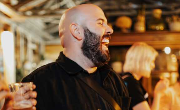 A man with a beard is holding a glass of wine.