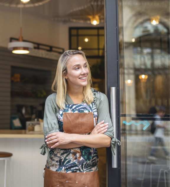 A woman with a brown apron is standing in front of a glass door at Ophelia on Queen Apartments, Kitchener