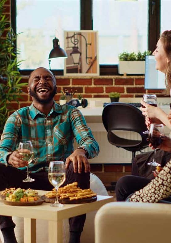 a group of people sitting in a living room eating and drinking wine