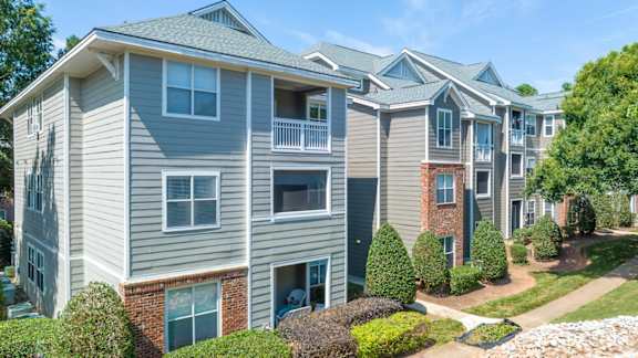 Apartment complex with grey and brown buildings and green bushes.