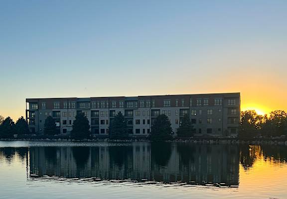a building on the lake at sunset with the sun setting behind it