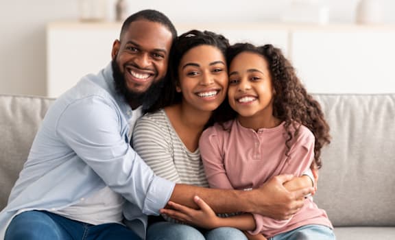 a family sits on a couch and smiles at the camera
