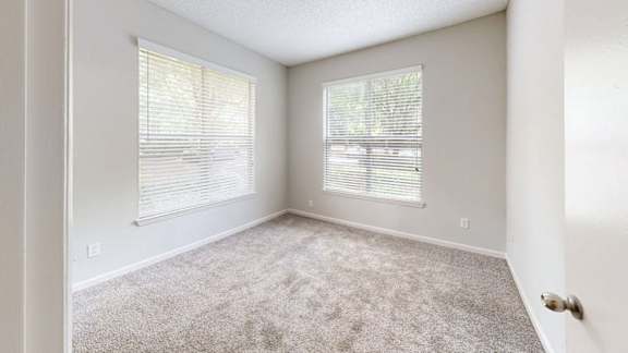 A room with carpeted floor and two windows with blinds.