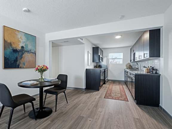 The Canvas Apartments dining room and kitchen with black table and chairs and open floor plan leading into a kitchen with dark wooden cabinets.