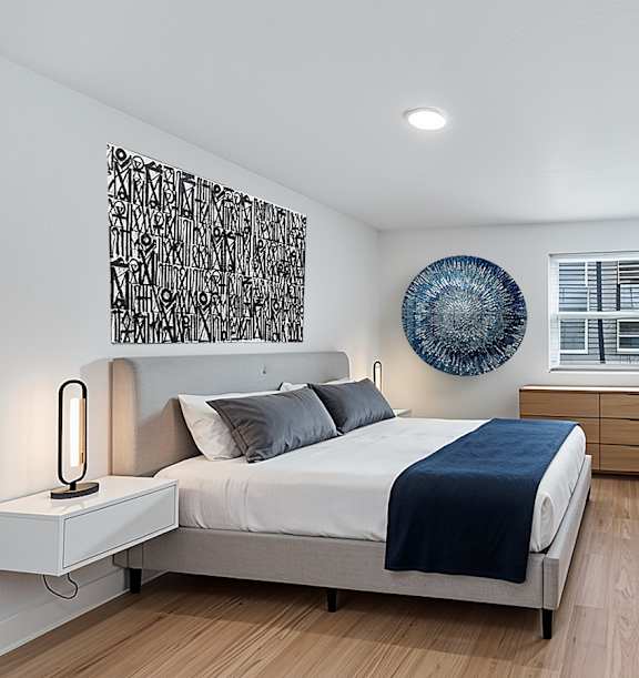 The Canvas bedroom one window, a dresser, and a bed with a black and white painting hung above it.