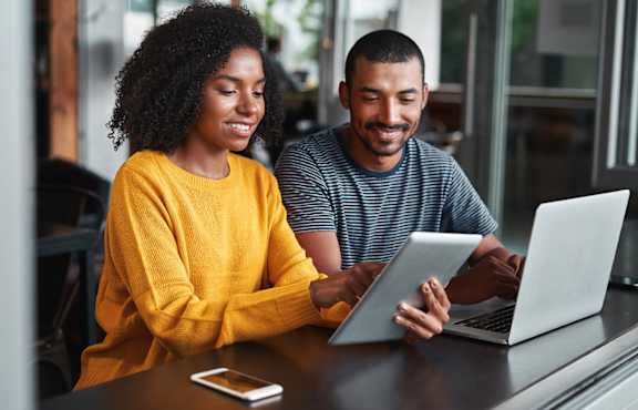 Two people are sitting at a table looking at a laptop.