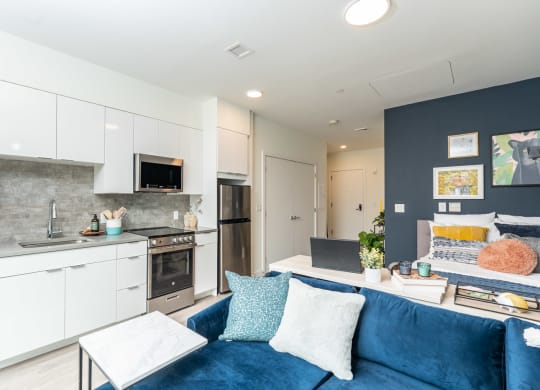 a living room with a blue couch and a kitchen with white cabinets and stainless steel appliances at Union 346, Somerville