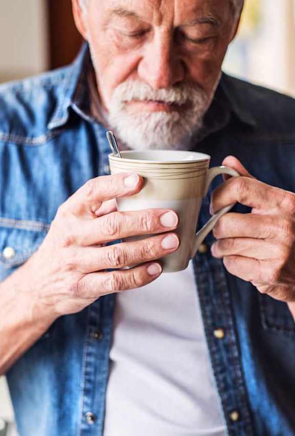 an older man drinking coffee from a cup in his kitchen