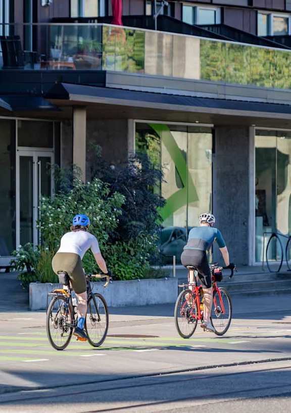 two people riding bikes down a street in front of a building