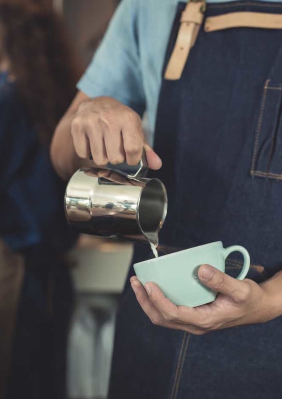 barista pouring milk into white coffee mug