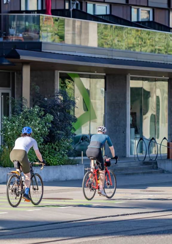 two people riding bikes down a street in front of a building