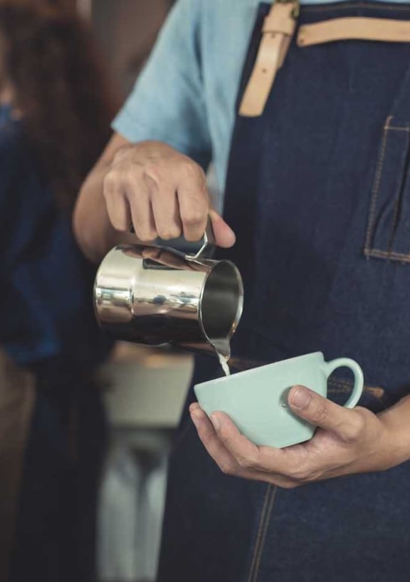 barista pouring milk into white coffee mug
