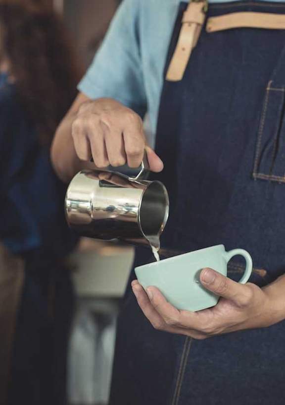 barista pouring milk into white coffee mug
