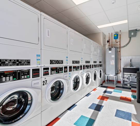 A row of washing machines are lined up in a laundry center.
