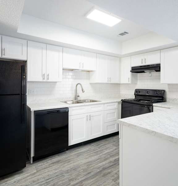 A black refrigerator is in a kitchen with white cabinets.