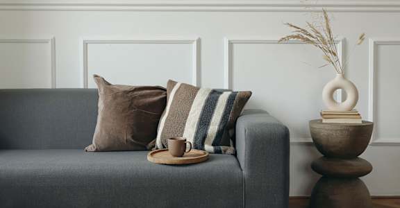 A grey couch with pillows and a vase on a wooden table.