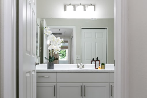 a bathroom with white cabinets and a white sink with a white orchid in a vase