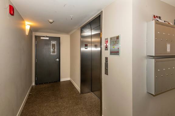 A hallway with a metal elevator and a metal door on the left.