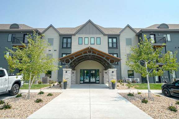 the front entrance of an apartment building with a driveway and trees