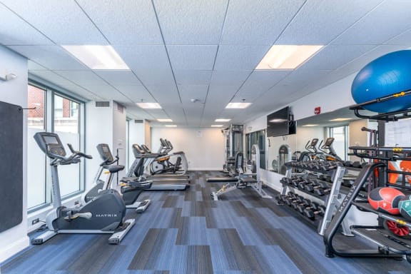 a gym with cardio equipment and weights in a building with windows