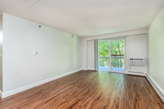 A room with wooden floors and a sliding glass door leading to a balcony.