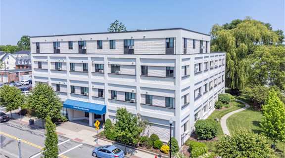 A modern building with a blue awning is surrounded by greenery and a clear blue sky.