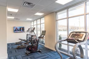 a gym with cardio equipment and large windows