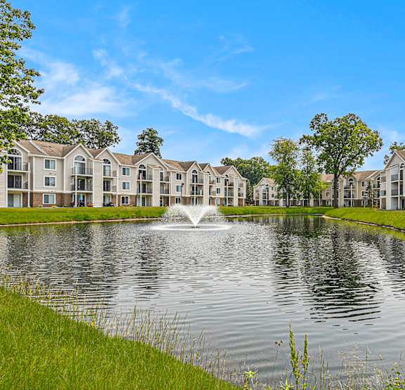 A fountain in the middle of a lake in front of apartment buildings at Orchard Lakes Apartments in Toledo, OH