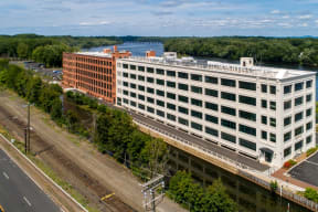 A large white building with a red brick section on the side is situated by a body of water. at Montgomery Mill Apartments in Windsor Locks, CT