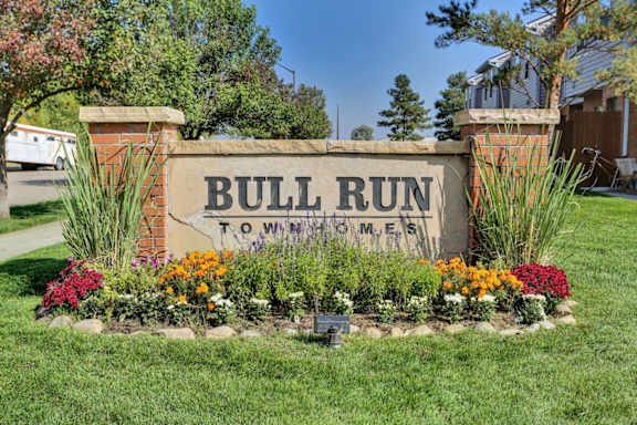 A sign that says Bull Run Towhomes in front of a grassy area.