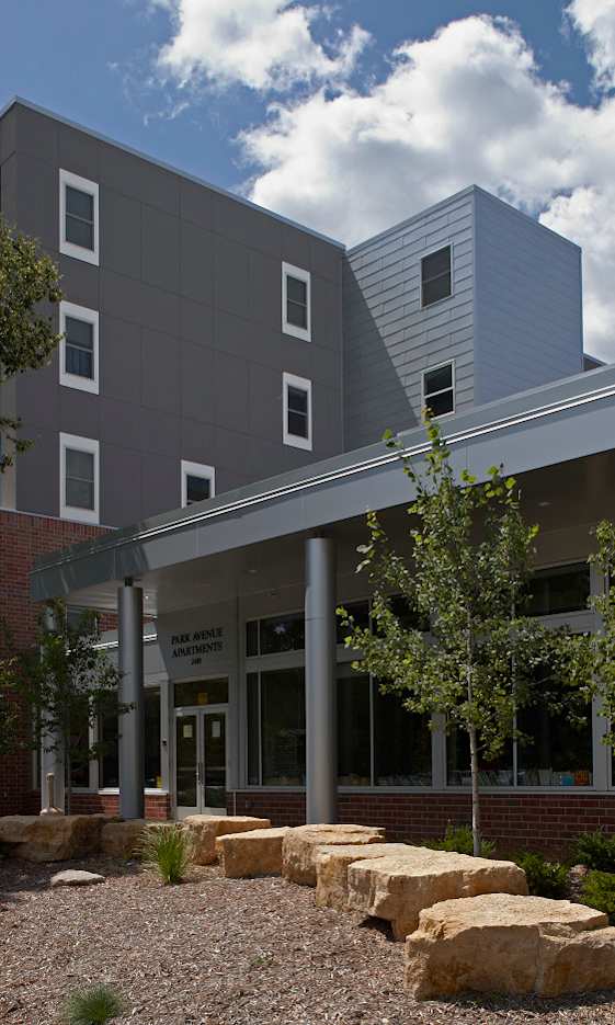 A modern building with a grey facade and a landscaped area in front.