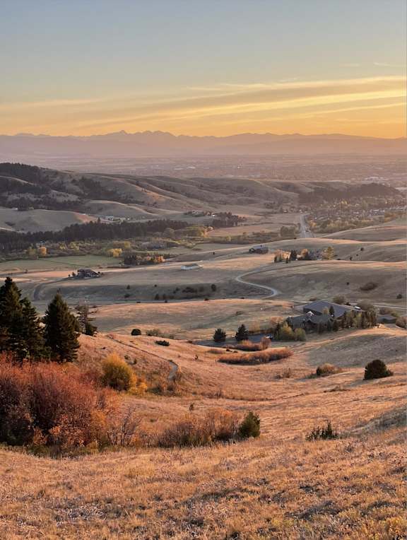 A serene landscape with a winding road and a house surrounded by trees and hills.