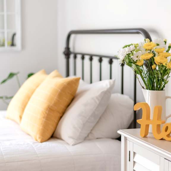 A white bedroom with a bed, nightstand, and a vase of flowers.