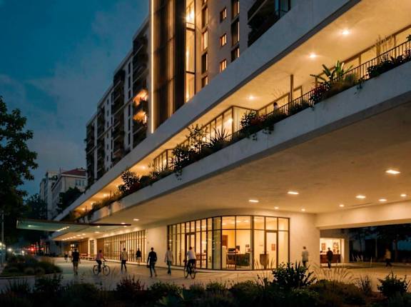 A modern building with balconies and people walking around outside at dusk.
