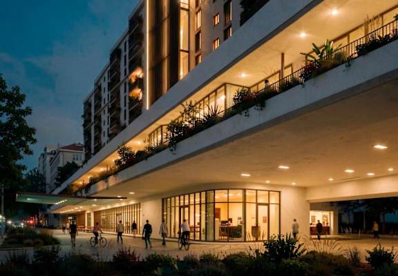 A modern building with balconies and people walking around outside at dusk.