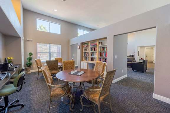 A room with a round table surrounded by chairs and a bookshelf filled with books.