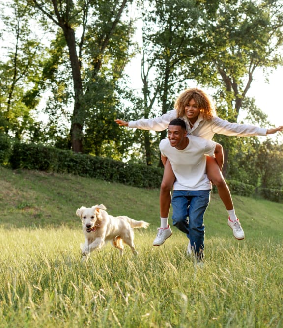 a man and woman running through a field with a dog