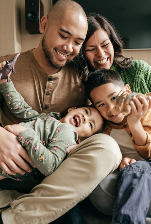 A family of four is sitting closely together, sharing a joyful moment. at Willow Grove Apartments , Colorado